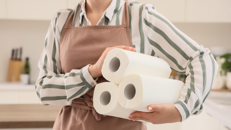 Woman in an apron holds three new rolls of paper towels.