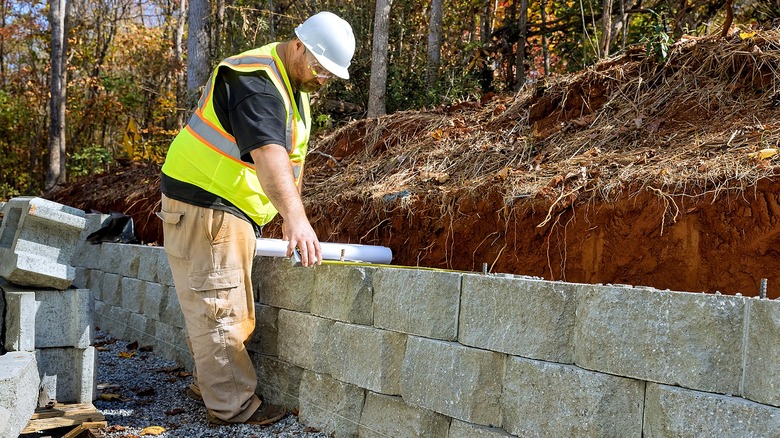 A professional in construction gear works on a concrete block retaining wall