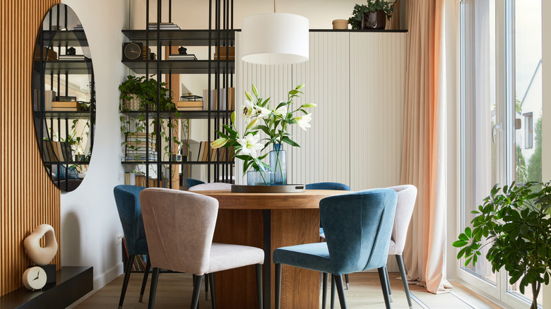 Modern dining room with round wood table, blue and white upholstered chairs, and wall mirror.