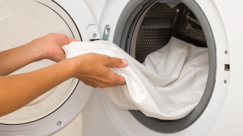 Hands placing white bed sheets in dryer