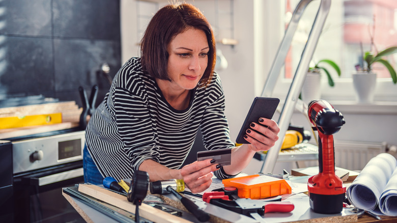 A person holding a credit card and shopping on their phone surrounded by tools
