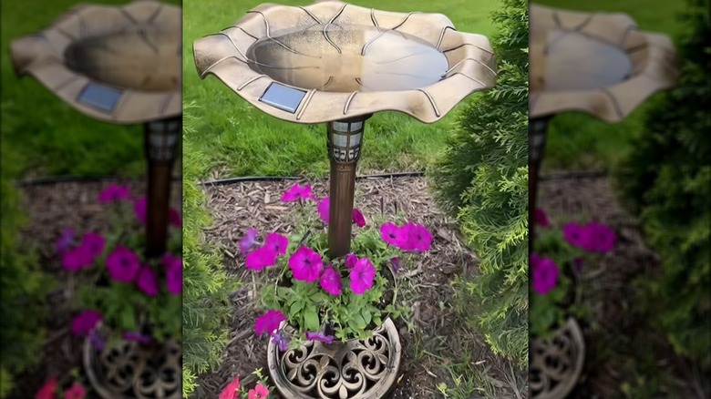 A plastic pedestal bird bath with a planter filled with flowers in a garden