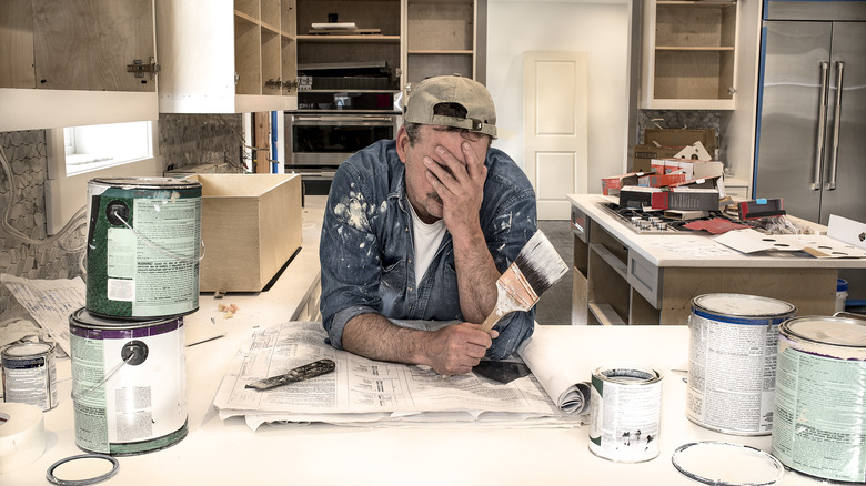 Person holding their face in their hands surrounded by paint cans and DIY mess