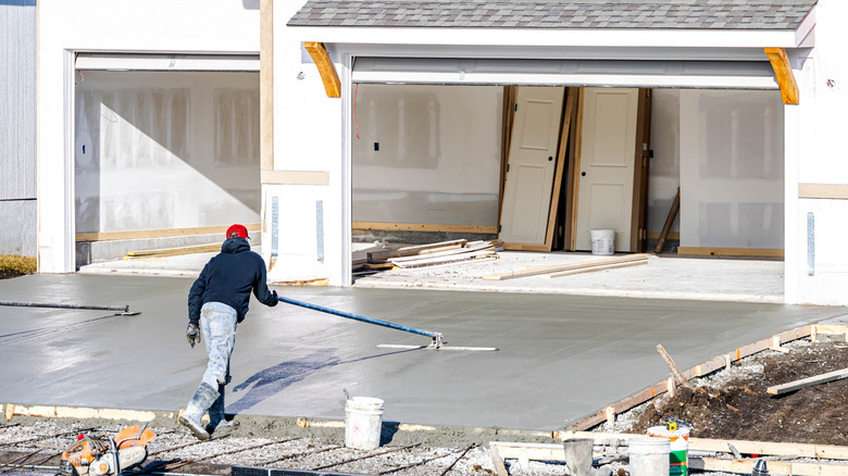 Worker leveling a poured concrete driveway in front of a home under construction