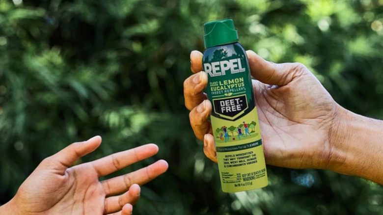 A dark-skinned hand passes a bottle of insect repellent to another person.