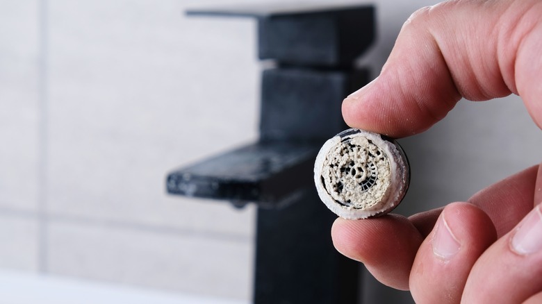 close up of person holding part of sink faucet with limescale buildup