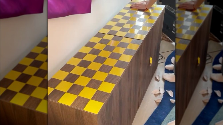 person adding yellow duct tape square to a brown wooden credenza