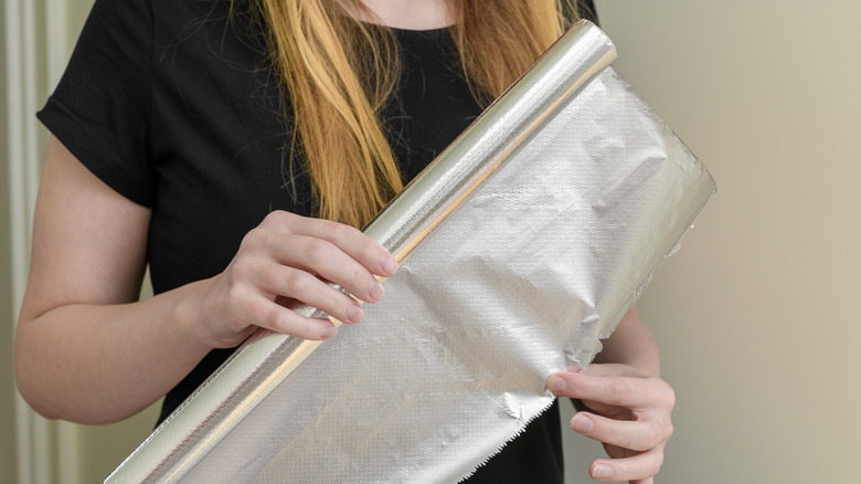 A woman unwinds aluminum foil from a roll