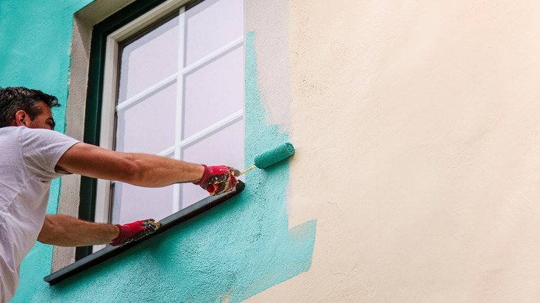 A person painting the outside of a home in a teal color