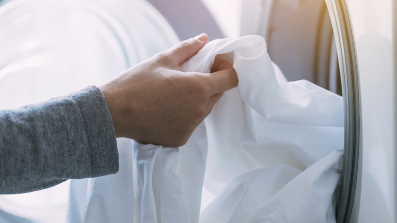A close-up of a person taking white laundry out of the washing machine