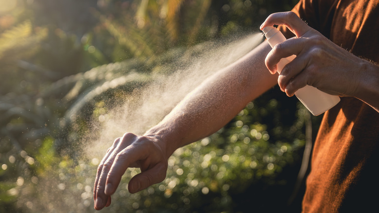 Man spraying arm with insect repellent