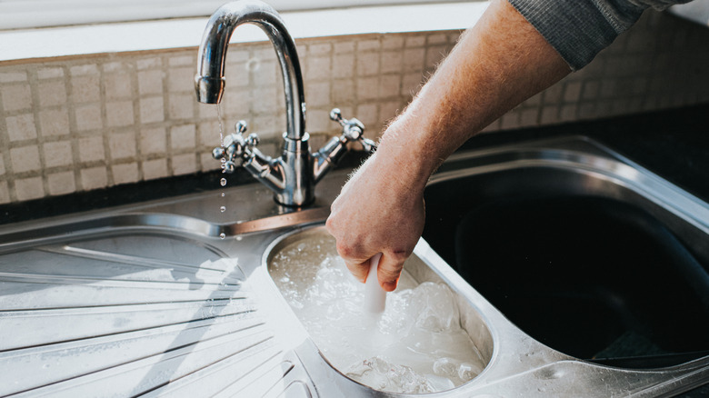 Man using a small plunger in kitchen sink