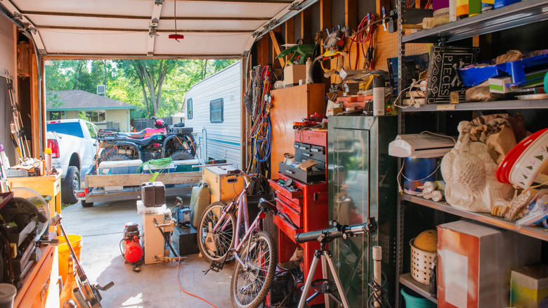 interior of cluttered garage looking out into driveway with truck, trailer, and RV