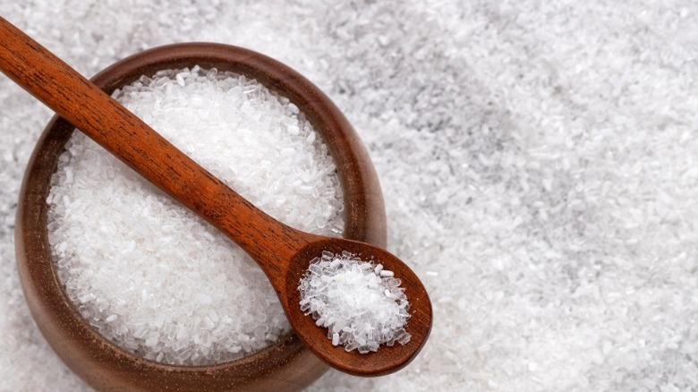 Epsom salt in a wooden bowl with a wooden spoon, spread out on a surface.