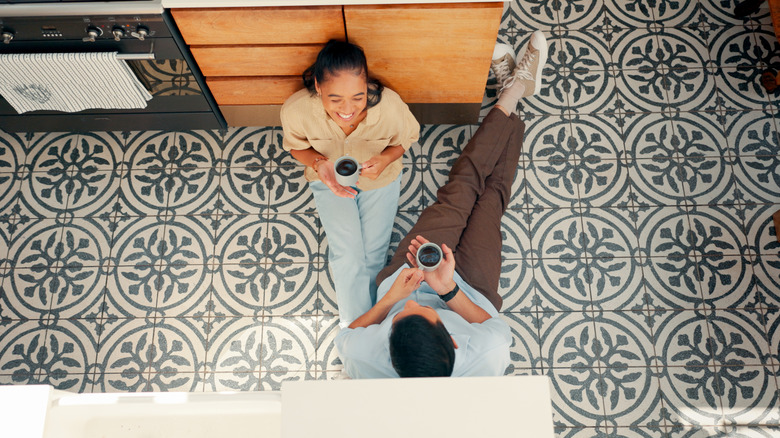 happy couple drinking coffee sitting on tile floor in kitchen