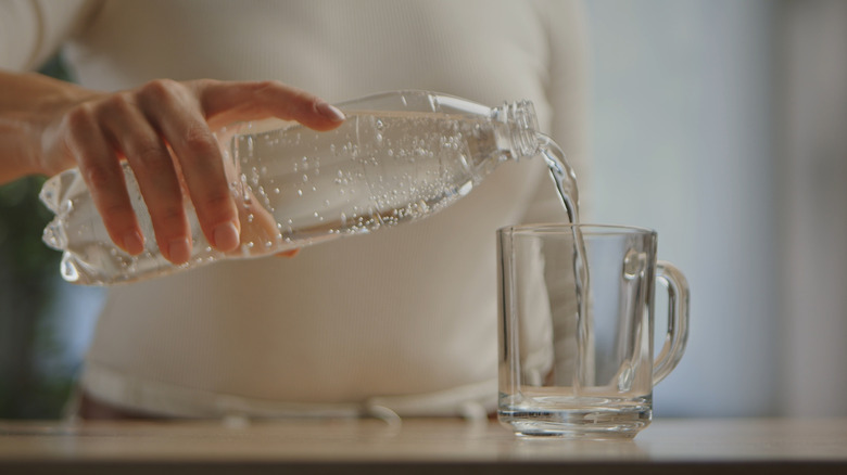 A person pours clear sparkling water from a bottle into a glass.