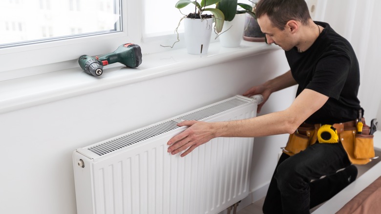 A repairman works on a white radiator
