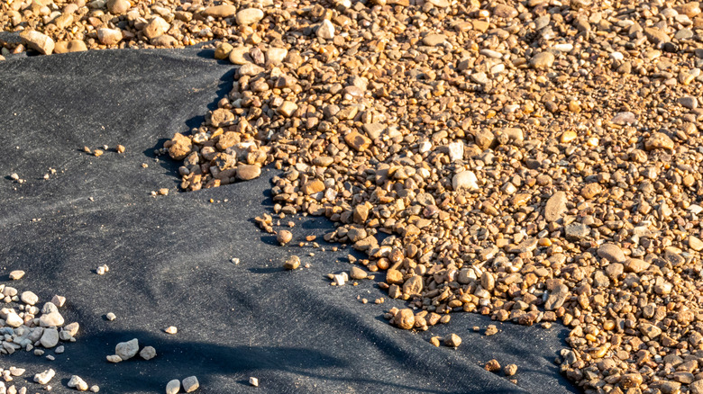 Laying landscape fabric under gravel to prevent weeds growing through
