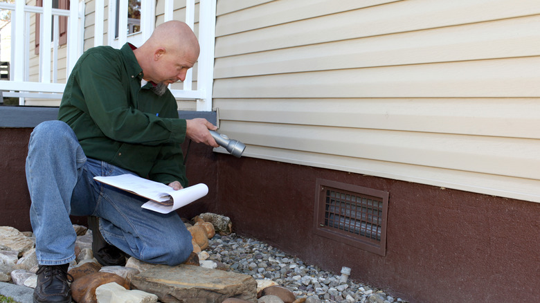 A person examining a home's foundation for damage