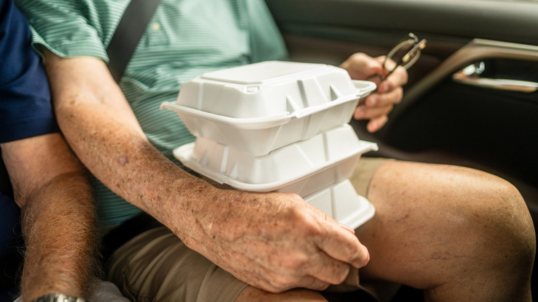 A man holds three takeout containers on his lap in a car