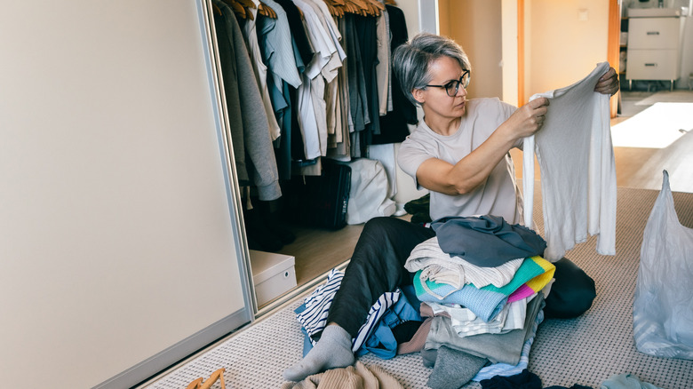 Woman sitting on the floor looking at clothes while decluttering closet