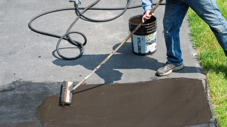 Man using a broom to spread asphalt sealer on blacktop driveway