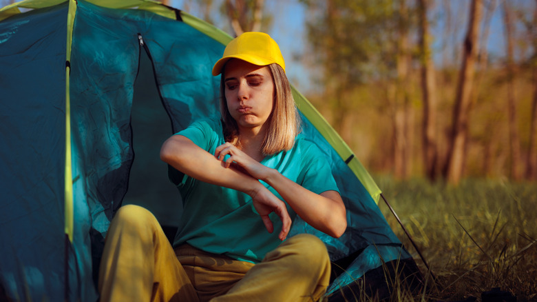 Woman sitting outside her tent scratching an insect bite