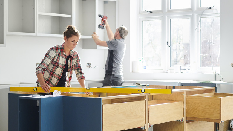 Two people installing kitchen cabinets