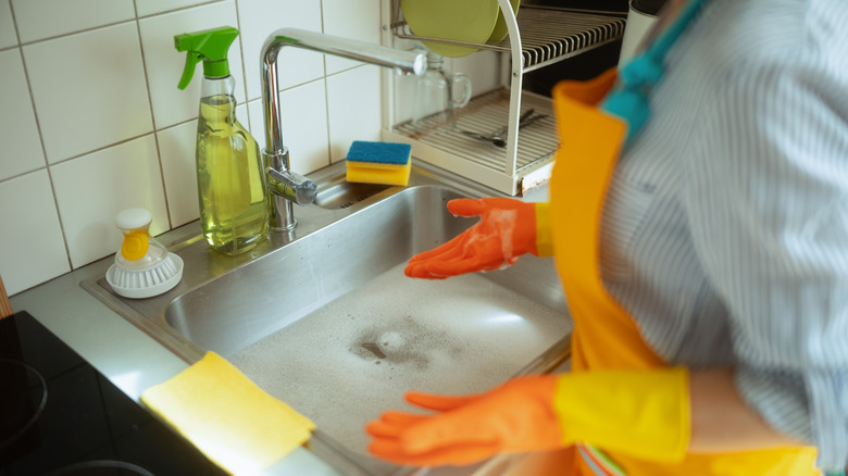 Woman stands over a clogged and smelly sink, trying to figure out the best way to unclog it.