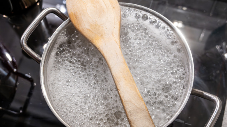 A wooden spoon on top of a pot a boiling water
