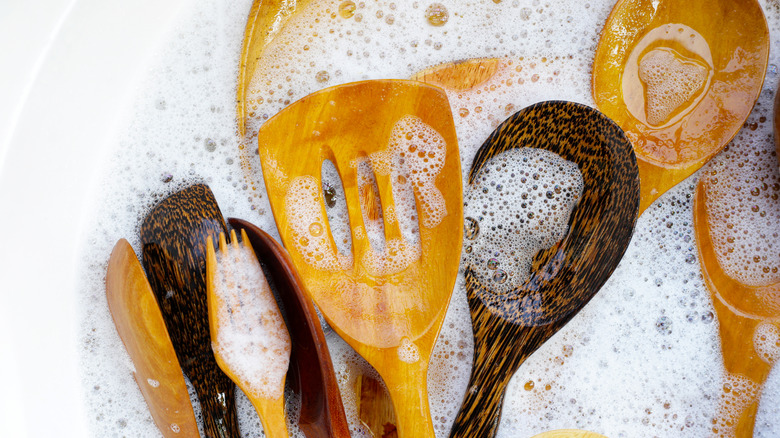 Wooden kitchen utensils sit in hot, soapy water