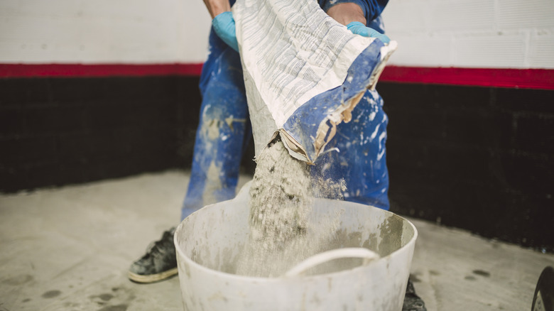 Someone pouring a bag of cement into a mixing bucket to make concrete