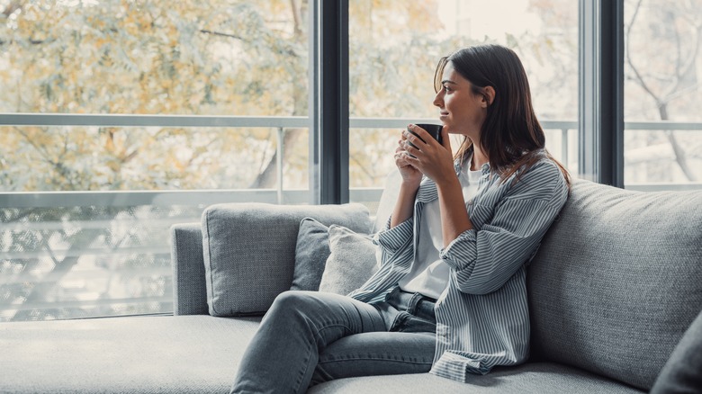 Cheerful dreamy girl holding mug of hot beverage, looking away in deep good thoughts