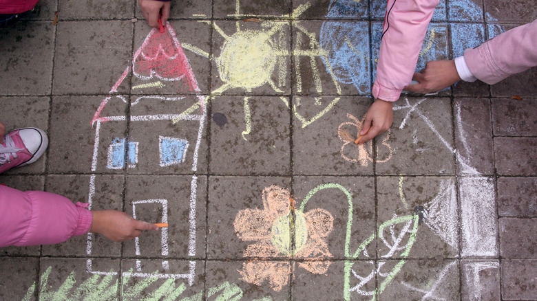 Drawing pictures of a house, sun, and flowers with sidewalk chalk
