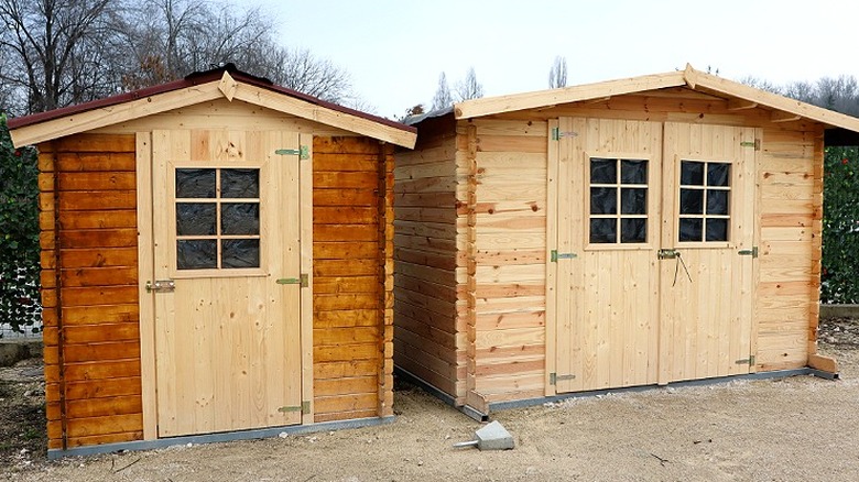 Two wooden storage sheds side by side outside surrounded by dirt