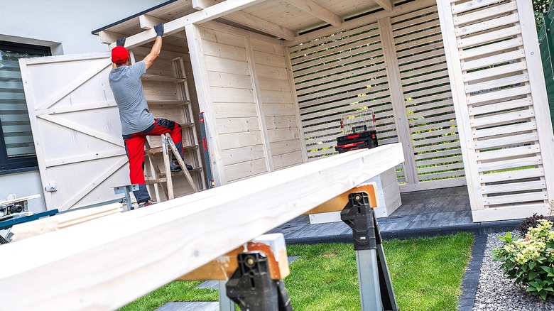 A person works on building a wood shed in a backyard