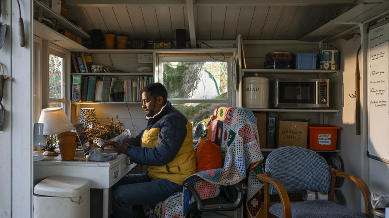 A man sits at a desk inside a cramped shed