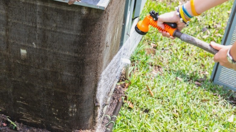 Person rinsing an A/C condenser with a garden hose