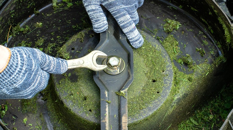Close-up of a person's gloved hands tightening a lawn mower blade nut