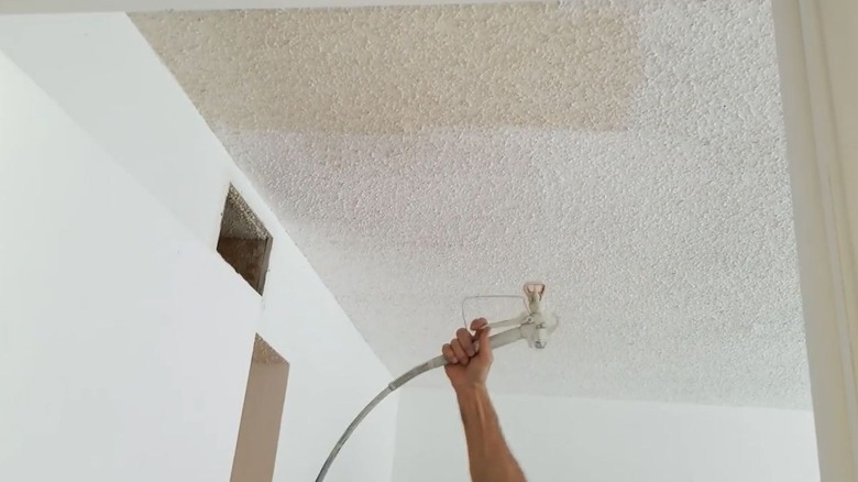 A person painting a popcorn ceiling with a sprayer