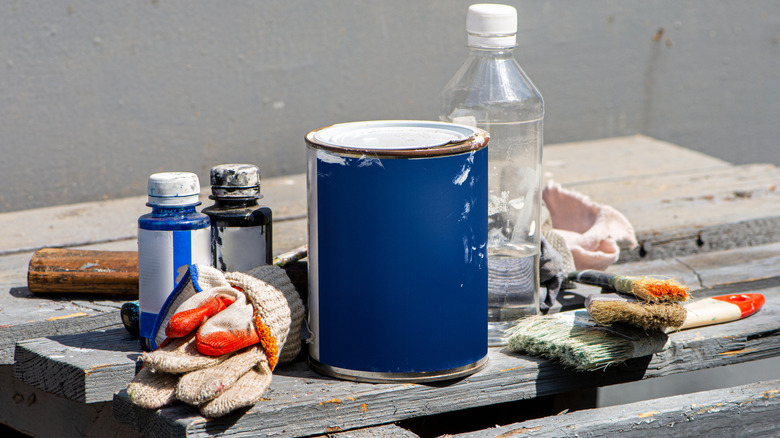 Various painting supplies like gloves and paint on a stack of wood
