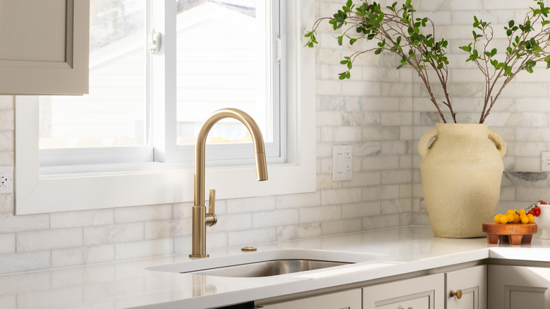 A gold kitchen faucet detail in a luxury kitchen with brown cabinets
