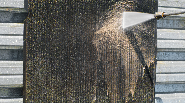 Pressure washing being used to clean a black and brown rug.