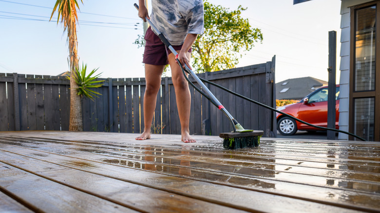 A person cleaning a deck by hand with a wet brush.