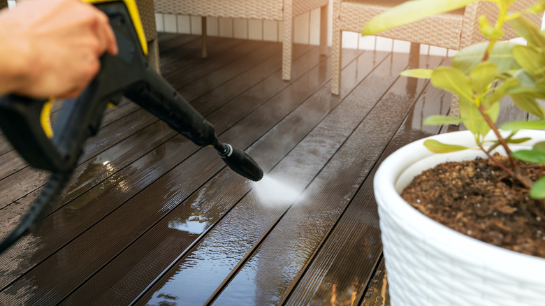 Man's hand holding pressure washer to wash composite decking
