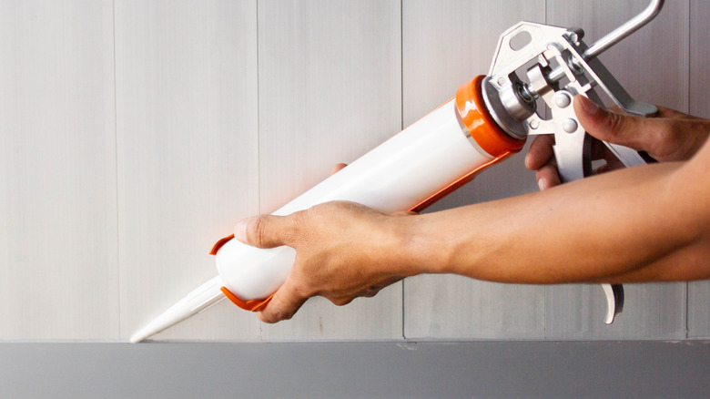 Man using caulk gun to seal home