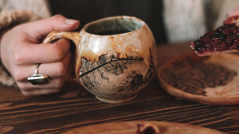 Close-up of a hand holding a handmade clay mug