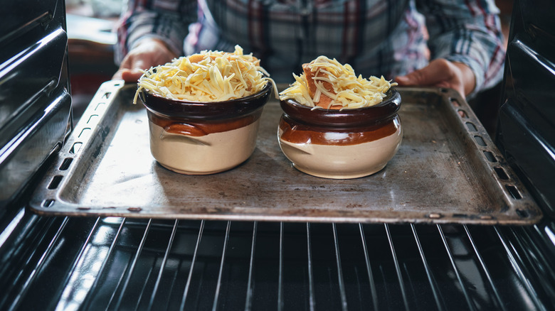Person places soup ramekins topped with cheese in oven.