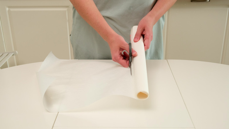 A person cuts a piece of parchment paper from a roll on a kitchen counter