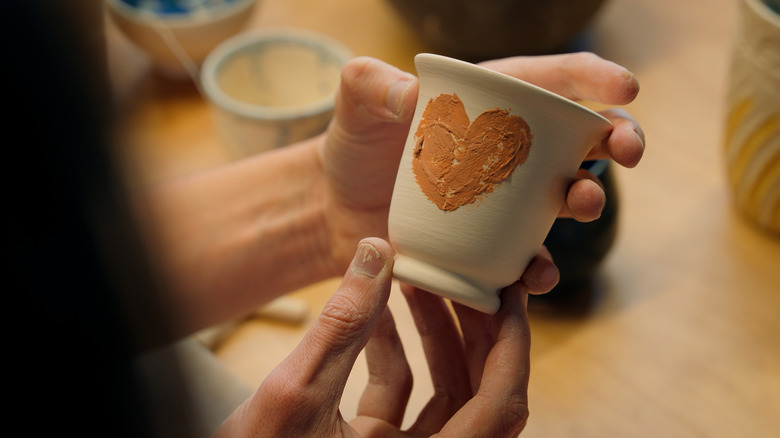 Hands holding a handmade, hand painted cup.